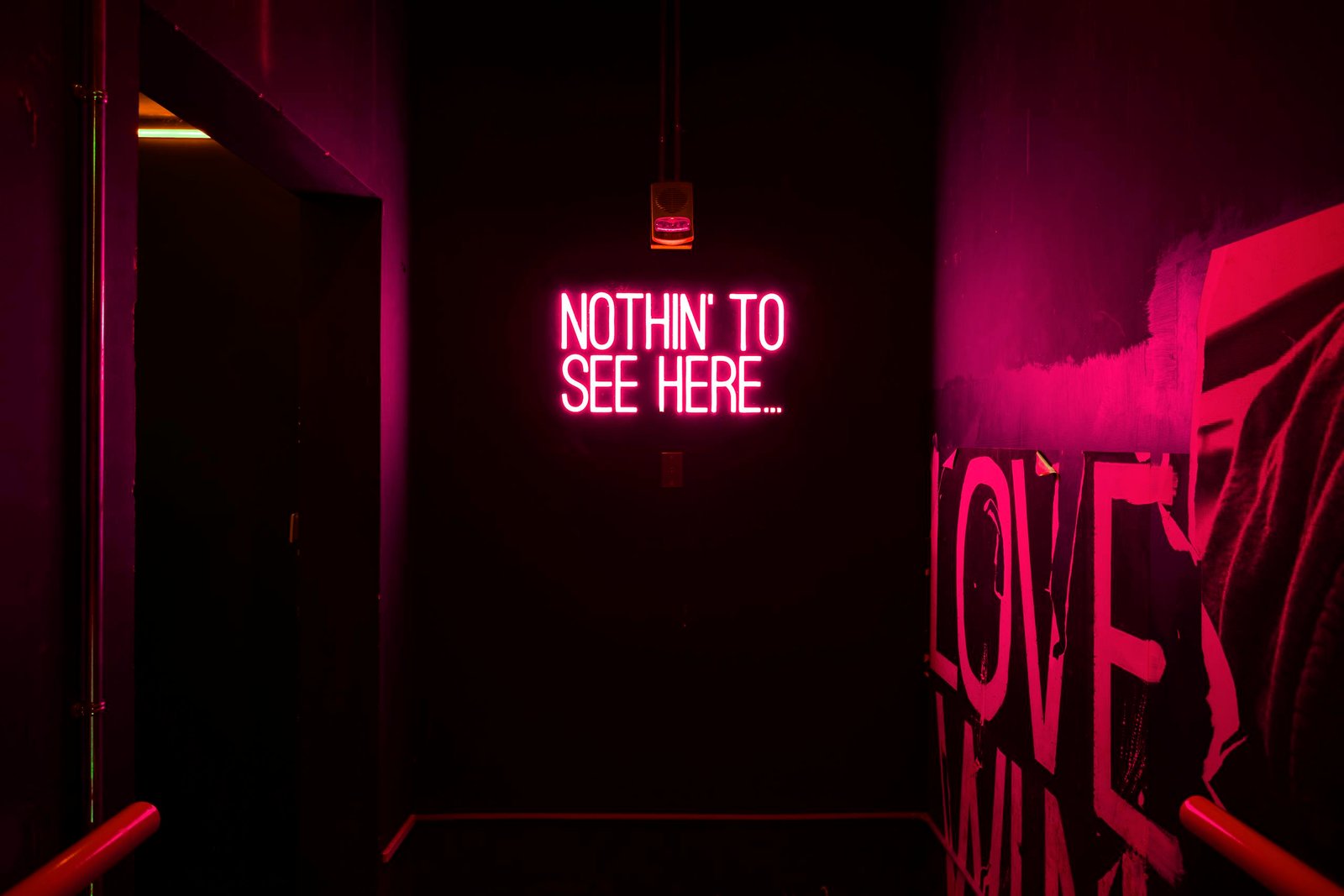 Neon sign reading 'Nothin' to see here...' in an artistic dark room.